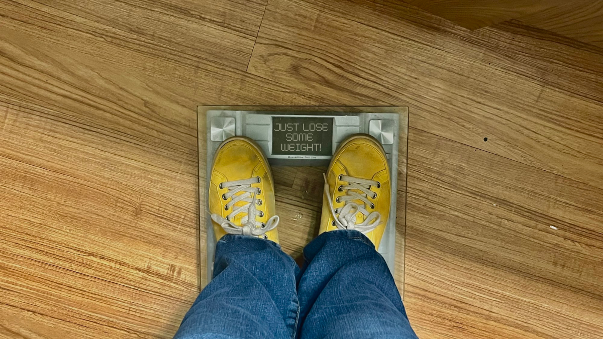 Image of a person standing on a scale, but instead of reading numbers the scale reads the common phrase, "just lose some weight."